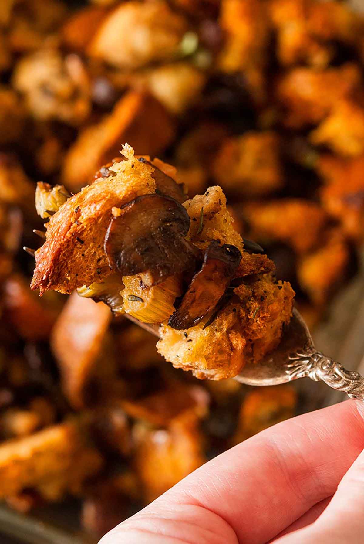 This traditional homemade bread stuffing recipe is moist and crunchy, flavorful and packed with earthy herbs and spices. The very best stuffing for turkey, duck, chicken or Cornish game hen! #stuffing, #recipes Fingers holding a fork-full of stuffing.