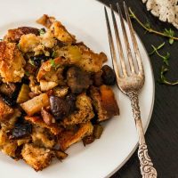 A plate of stuffing with a victorian-style fork on a black table with a lave table cloth and a few sprinkles of thyme.