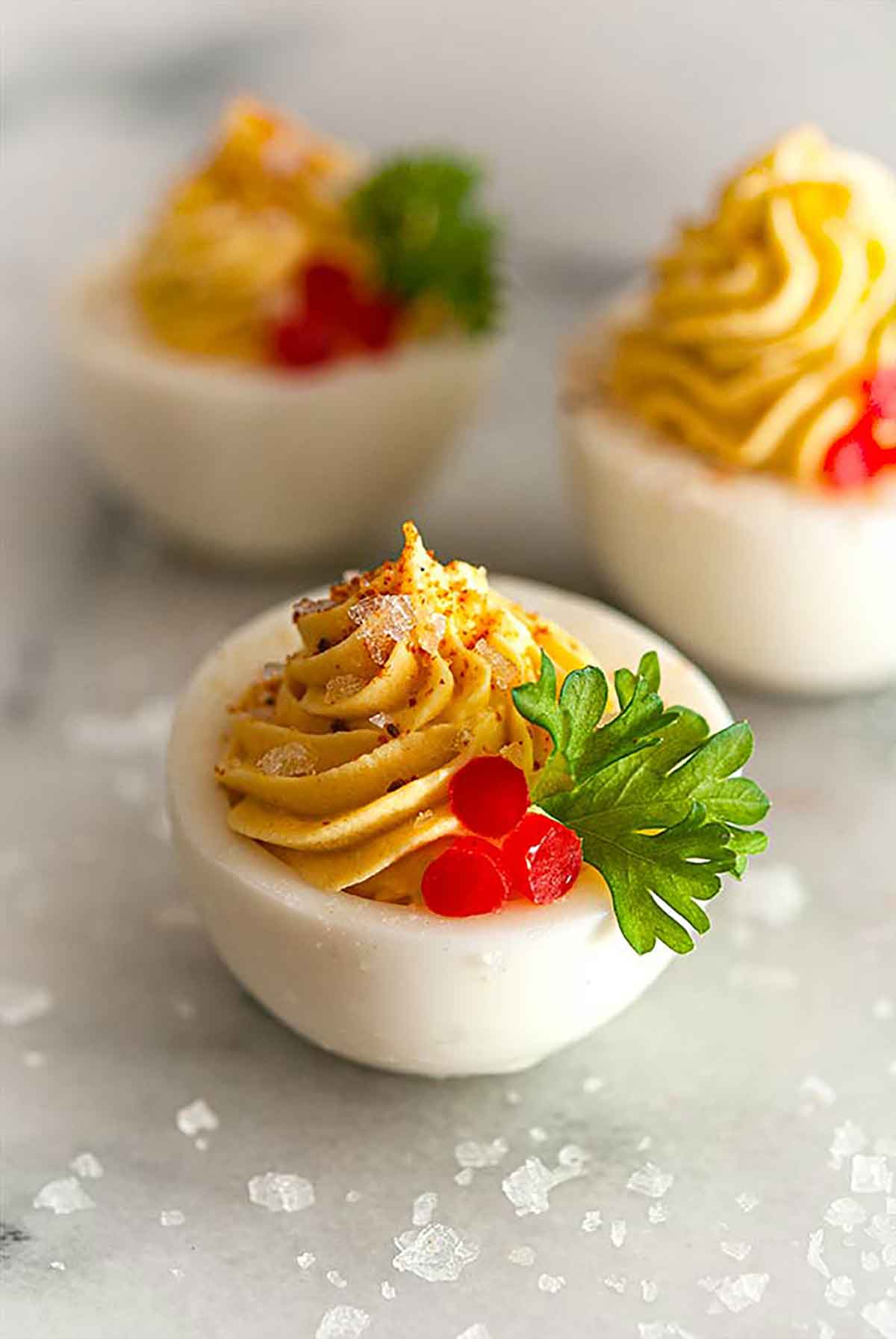 3 deviled eggs on a marble slate, sprinkled with salt, garnished with bell pepper and cilantro.