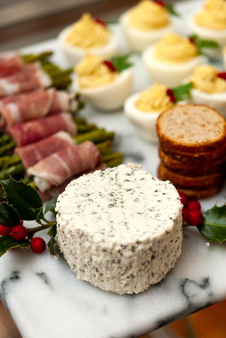 A cheese plate with cheese, prosciutto-wrapped asparagus, deviled eggs, crackers and holly. 