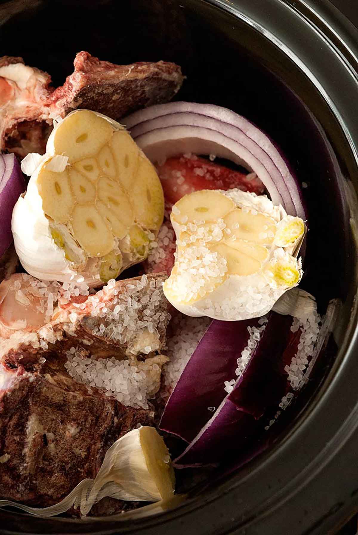 A crockpot filled with garlic, onions, salt and bones.