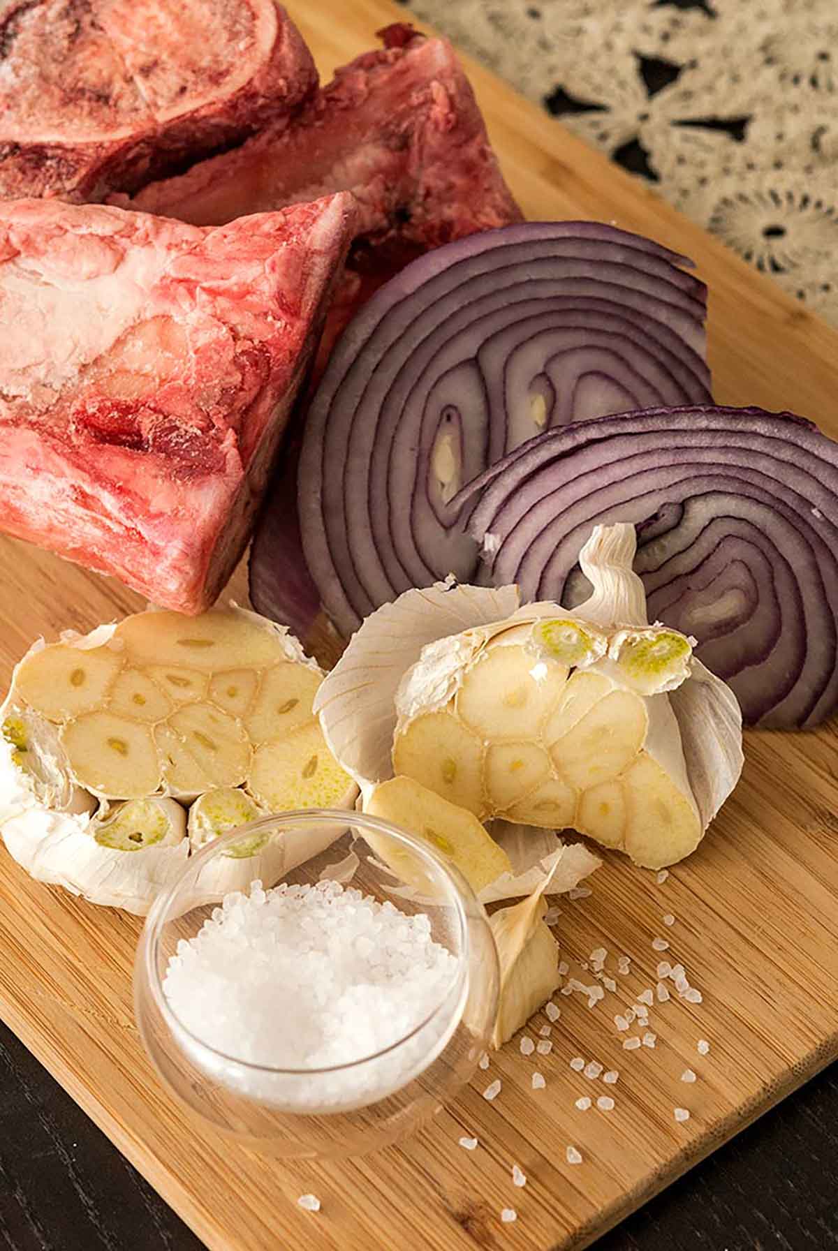 A cutting board with cut garlic, onions and a bone.