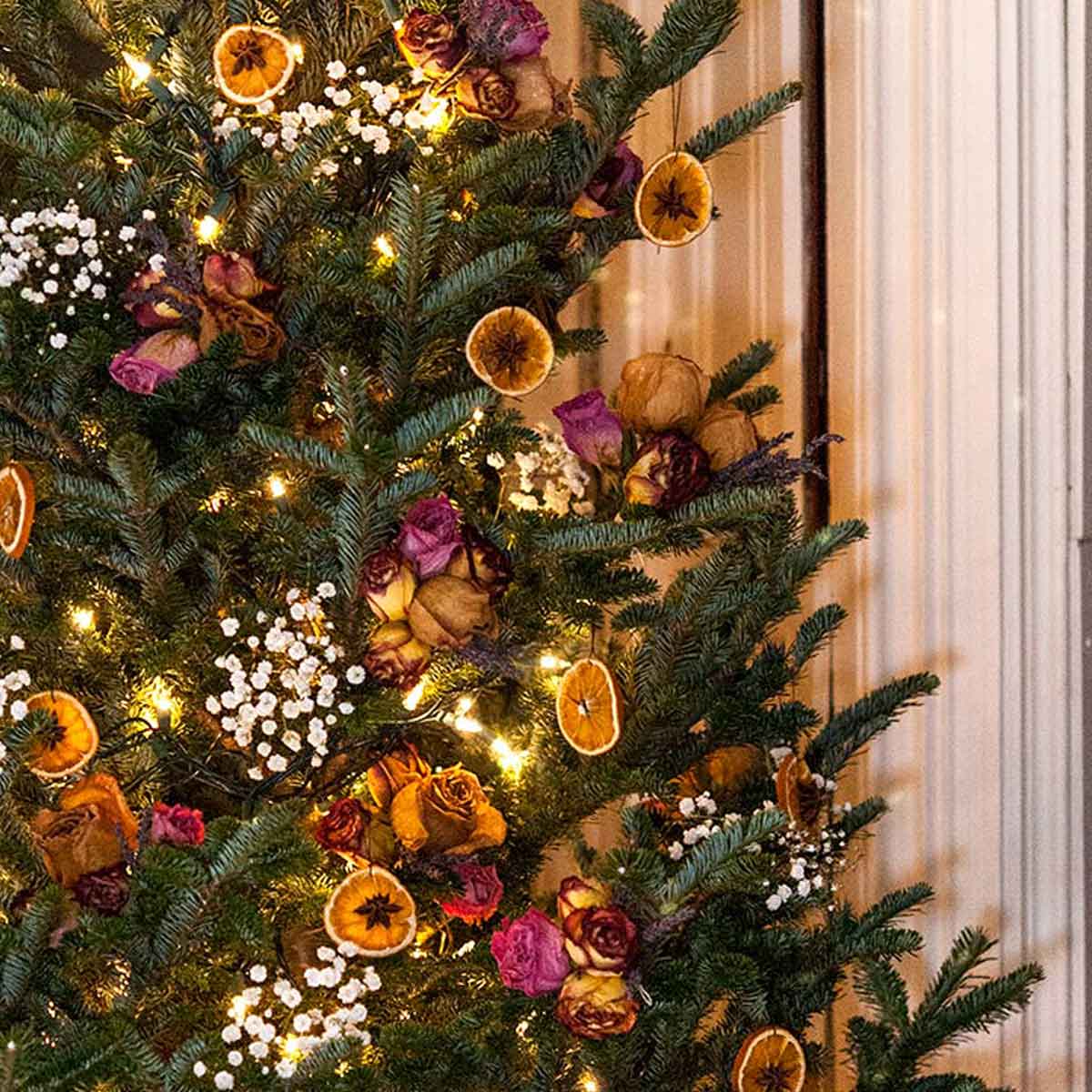 A colorful Christmas tree decorated with flowers and dry orange ornaments.