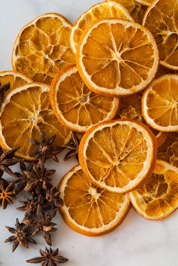 Dry orange slices and star anise piled on a white marble table.