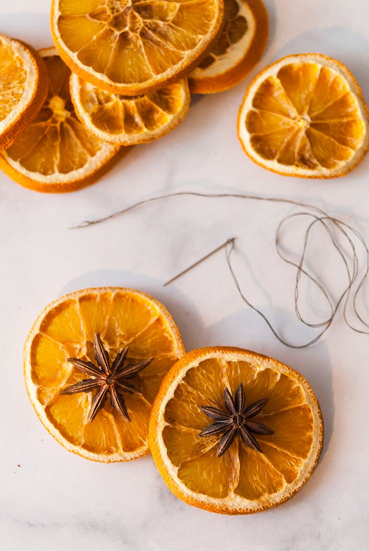 2 dry orange slices on a white marble table next to a needle and thread.