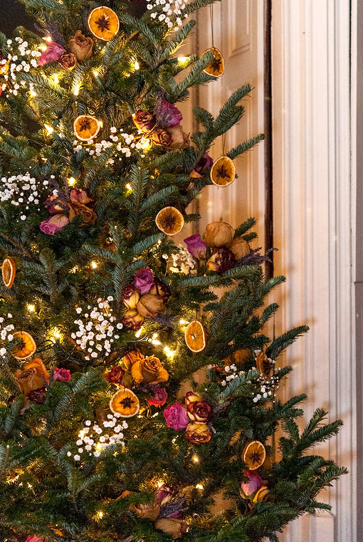 Un arbre de Noël coloré décoré de fleurs et d'ornements orange secs.