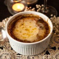 A bowl of French onion soup on a lace table cloth beside candles.