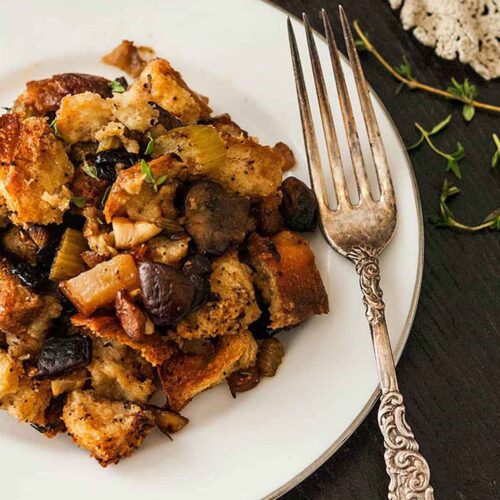 A plate of stuffing with a victorian-style fork on a black table with a lave table cloth and a few sprinkles of thyme.