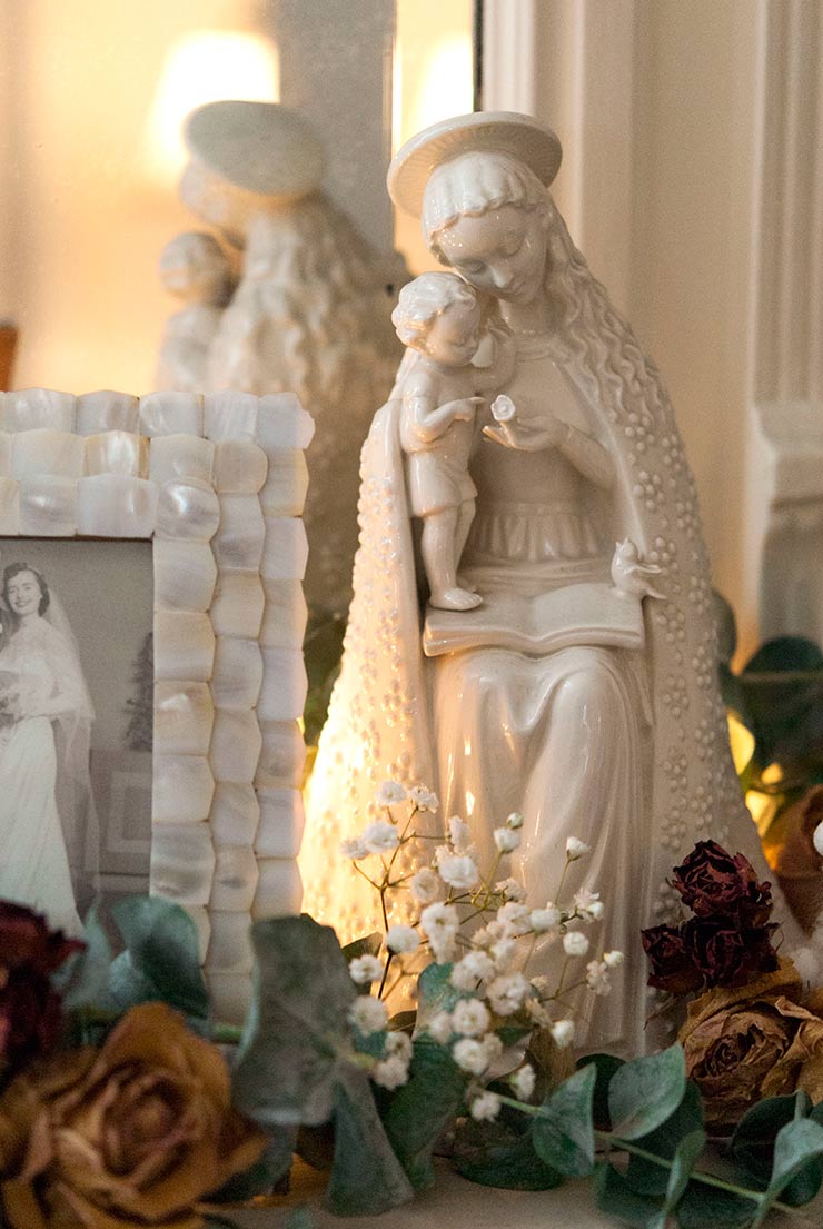 A small madonna statue next to a picture frame of a vintage marriage, with dry flowers below.