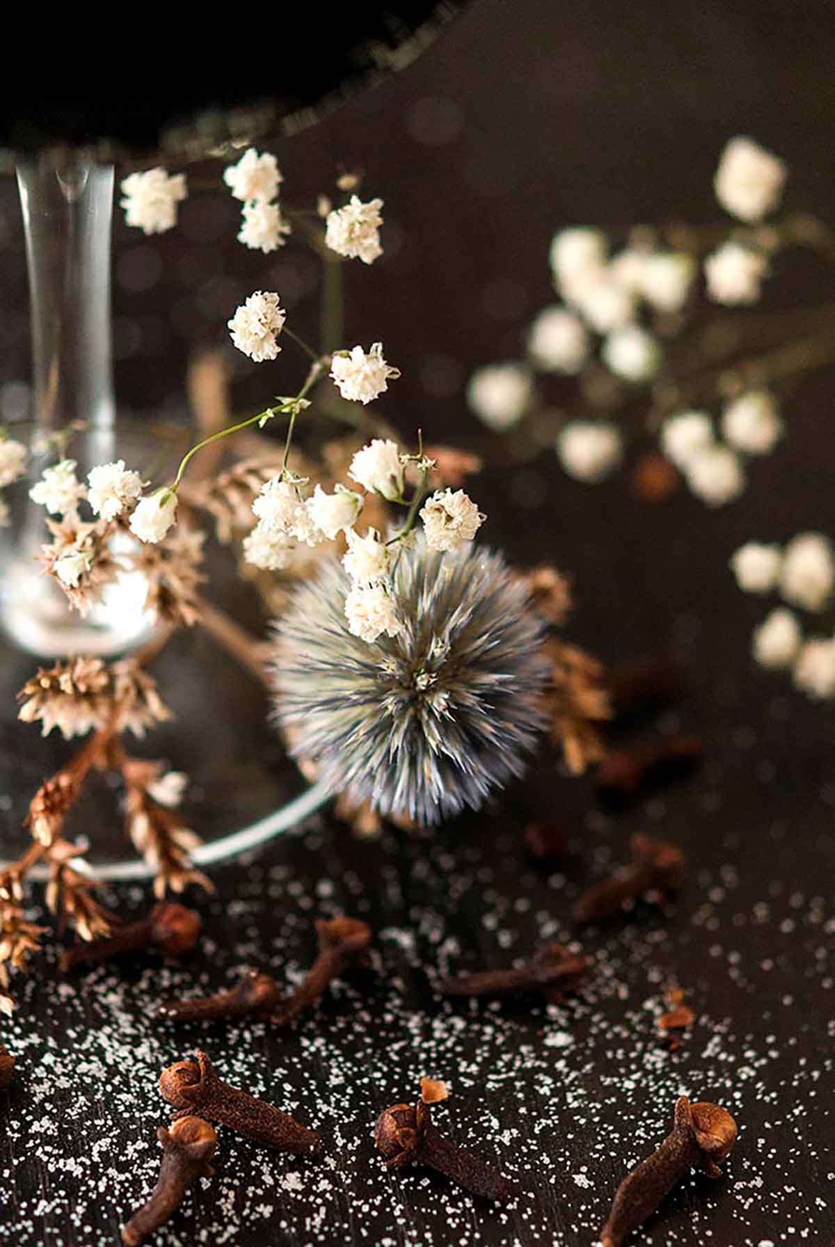 A few dry flowers at the base of a cocktail glass on a black table sprinkled with sugar.