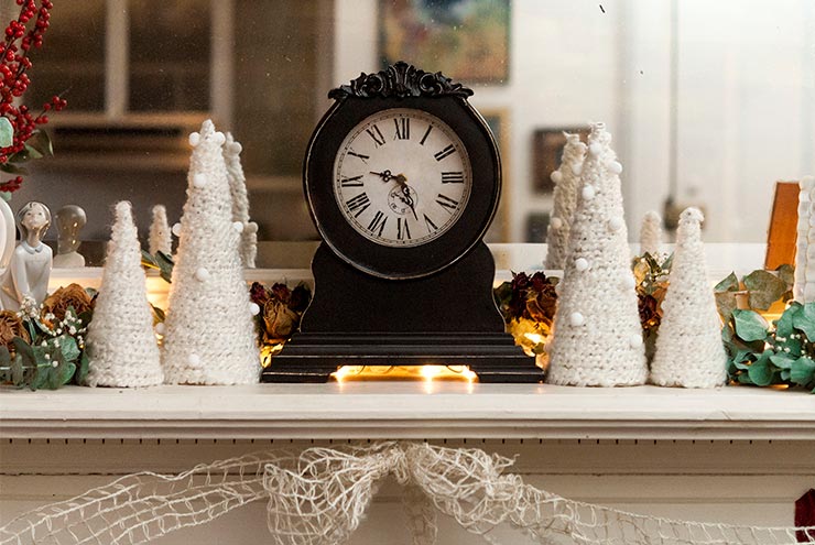 Small Christmas trees made of yarn on a mantle decorated with dry roses, eucalyptus and a Victorian clock.