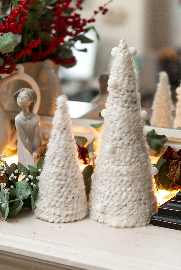 Small Christmas trees made of yarn on a mantle decorated with dry roses and eucalyptus.