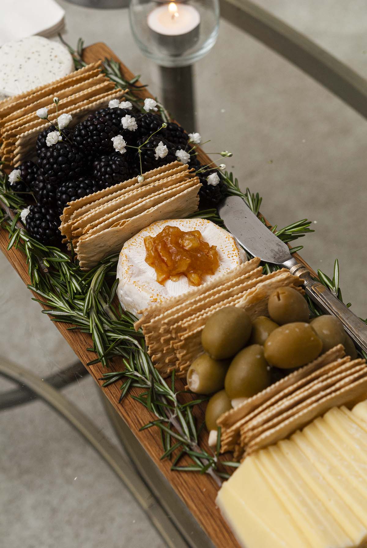 A cheese board with cheese, olives, berries, crackers and rosemary.