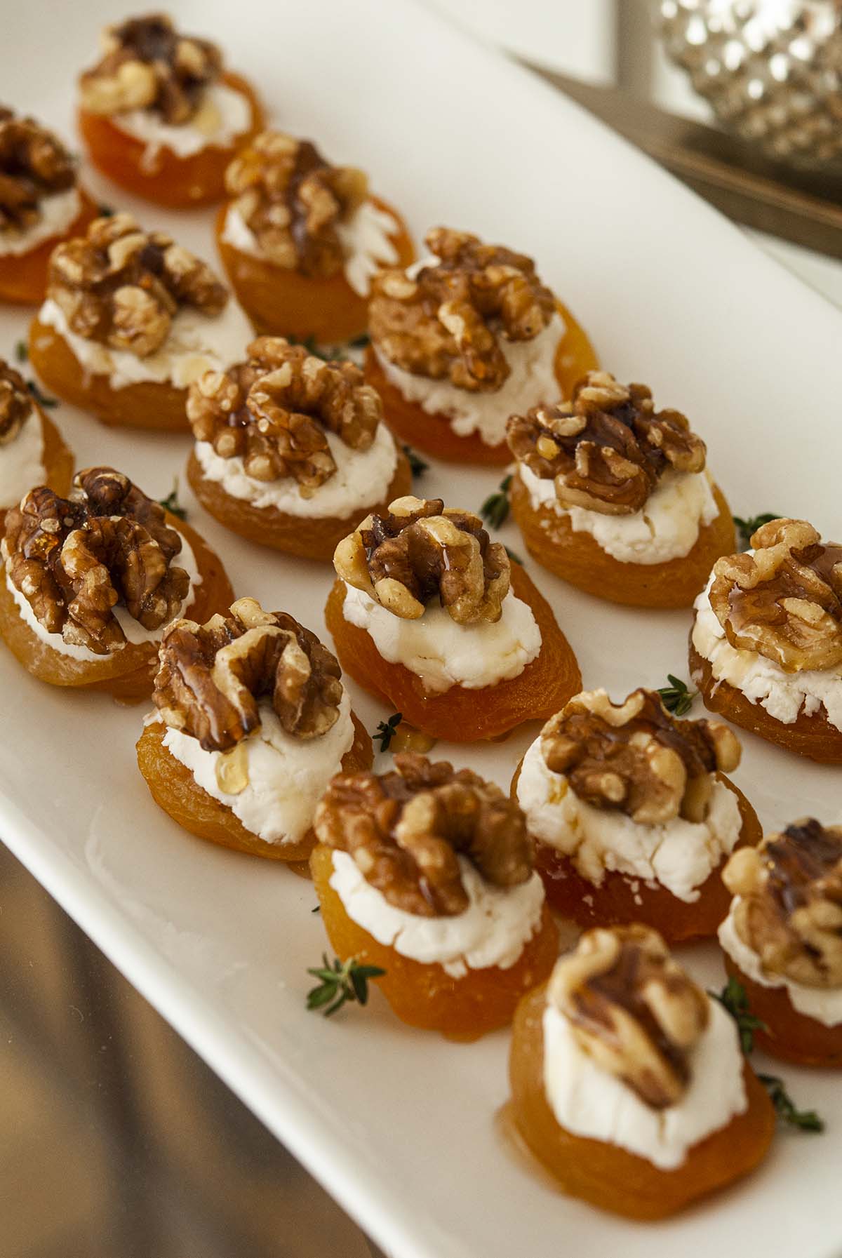 About 16 apricot appetizers with cheese and nuts on a plate.