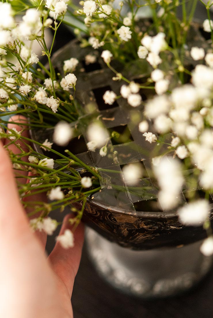 A grid made with masking tape on a vase with baby's breath stuck in the grid.