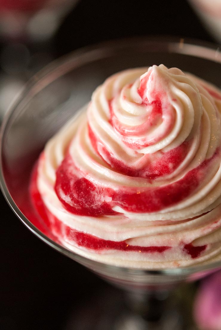 White chocolate mousse with raspberry swirls in a small glass.