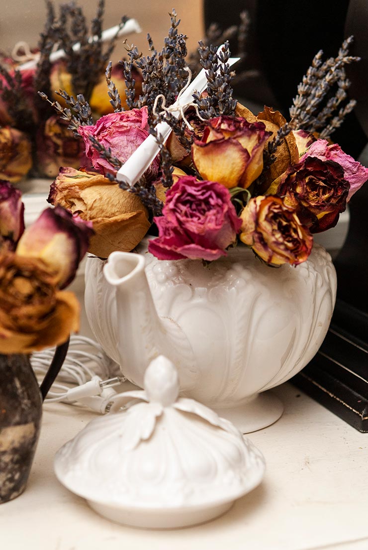 A tiny, paper scroll tied with string, sitting on top of a tea kettle filled with flowers.