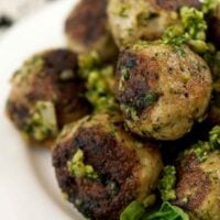 Pesto covered meatballs on a plate, garnished with basil.