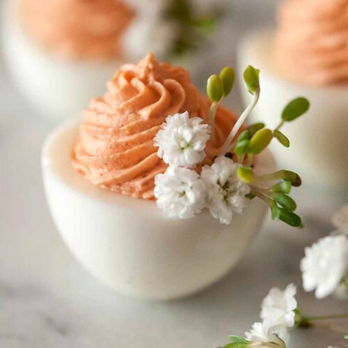 3 deviled eggs on a marble table with pink filling and garnished with baby's breath and sprouts.