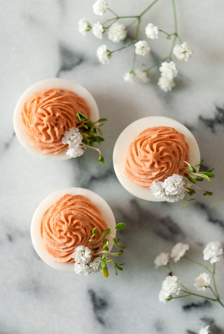 3 deviled eggs on a marble table with pink filling and garnished with baby's breath and sprouts.