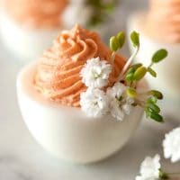 3 deviled eggs on a marble table with pink filling and garnished with baby's breath and sprouts.