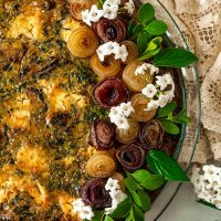 A quiche, garnished with pearl onion roses and little flowers with a lace tablecloth wrinkled at its side.