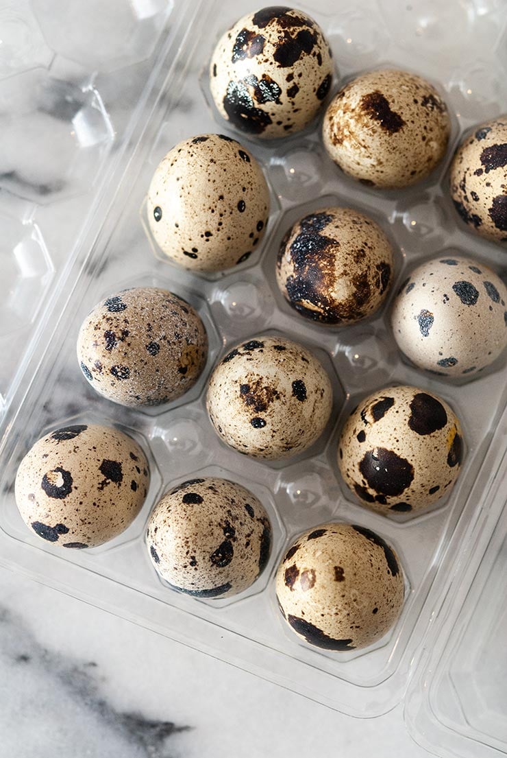 12 quail eggs in a plastic package on a marble table.