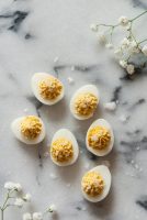 6 deviled quail eggs garnished with flake salt on a marble table with baby's breath flowers in the corners.