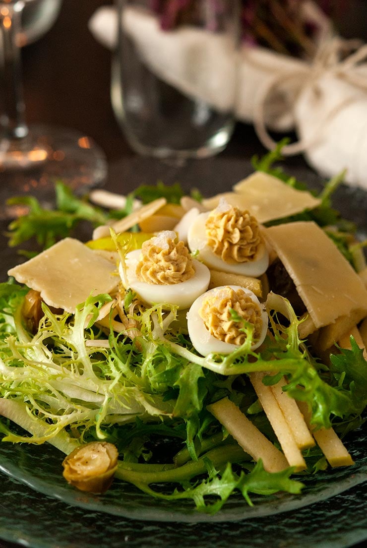 Deviled quail eggs in a salad on a dark table with glassware.