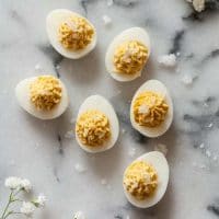 6 deviled quail eggs garnished with flake salt on a marble table with baby's breath flowers in the corners.