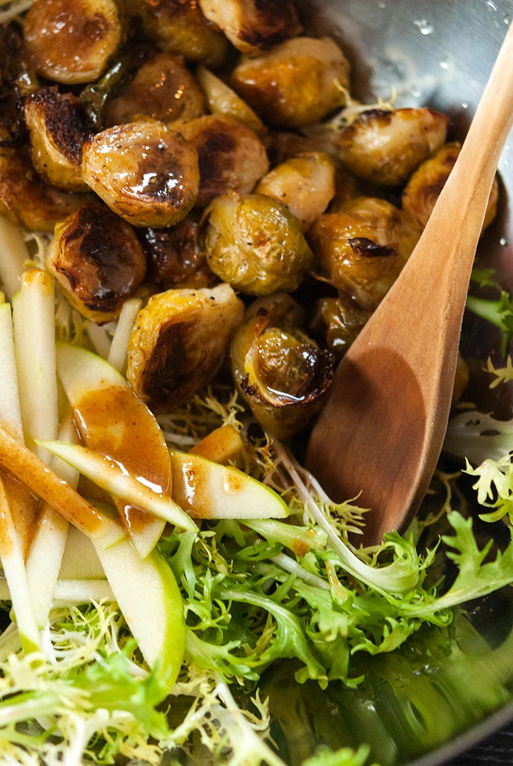 A large bowl of Brussels sprouts, diced green apple, frisée and a wooden spoon.