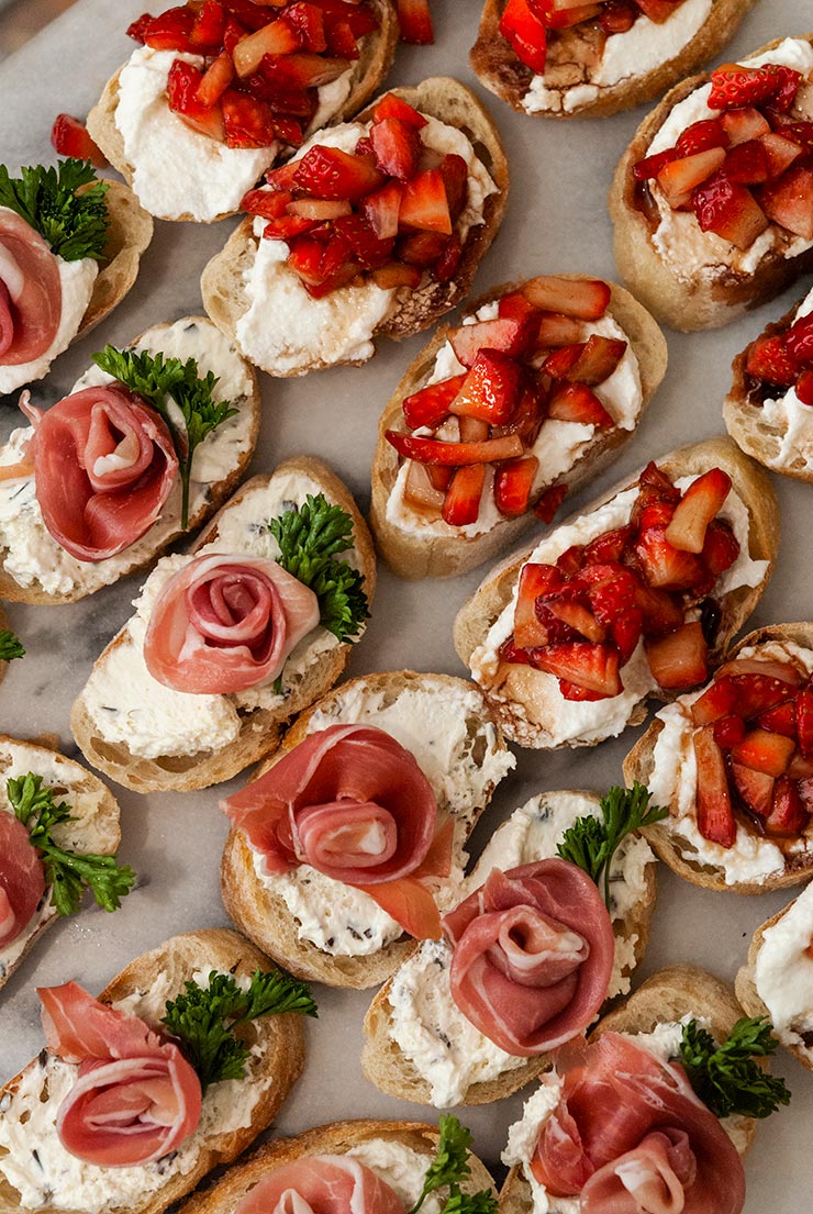 Assorted strawberry and prosciutto rose crostini on a marble plate.