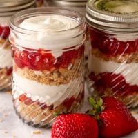 Strawberry rhubarb cups with vanilla cheesecake mouse on a marble table with a few strawberries beside them.