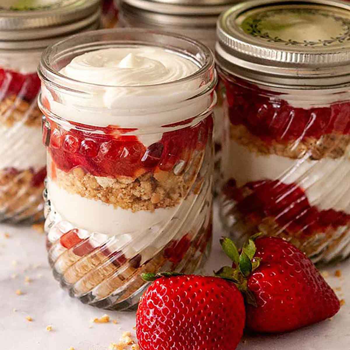 Strawberry rhubarb cups with vanilla cheesecake mouse on a marble table with a few strawberries beside them.