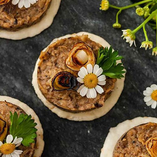 4 mushroom pâté canapés garnished with scallions and flowers on a marble slate.