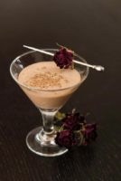 A small glass of Mexican Chocolate liqueur on a table, garnished with a dry rose with 3 roses at its base.