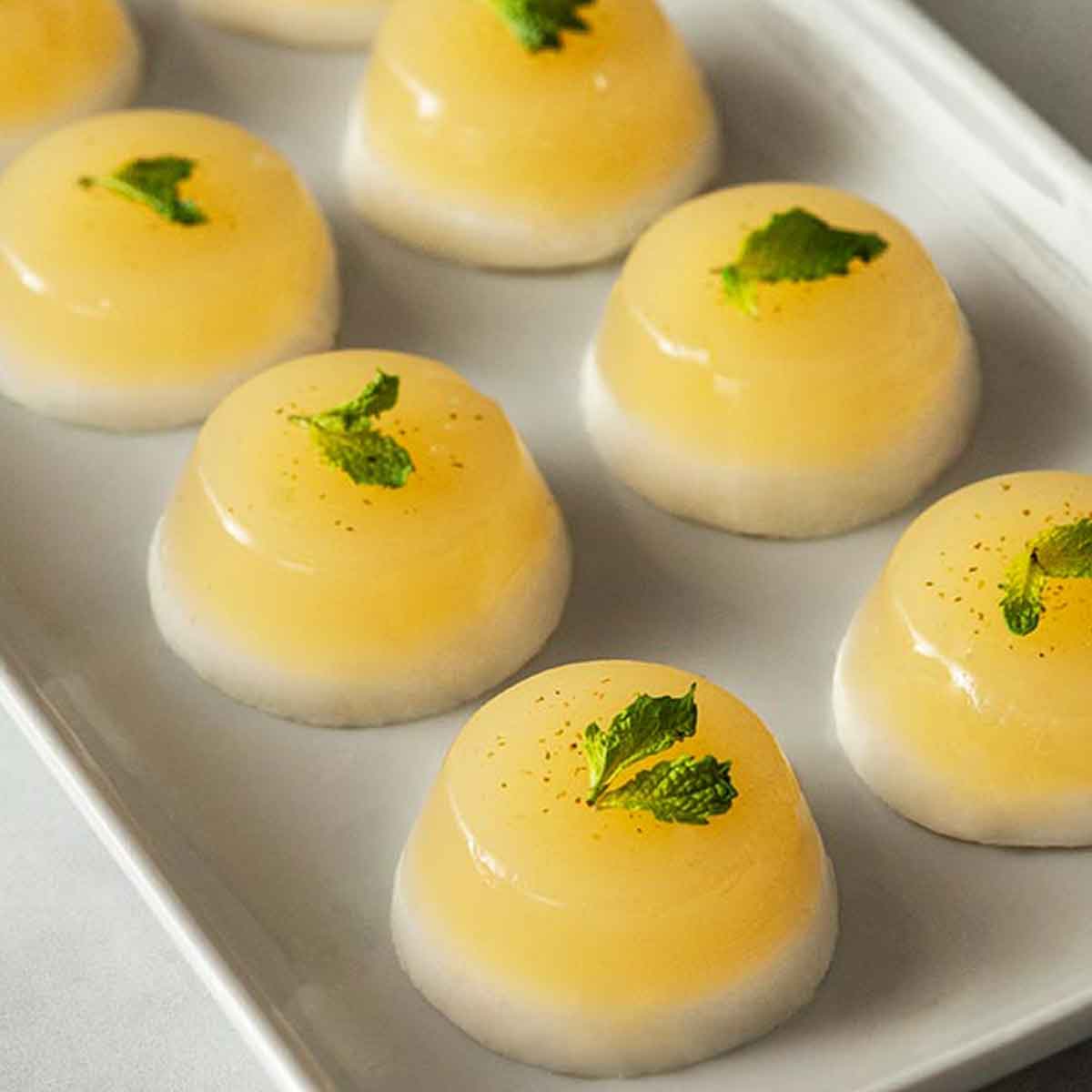 8 coconut mojito jello shots on a plate, garnished with mint.