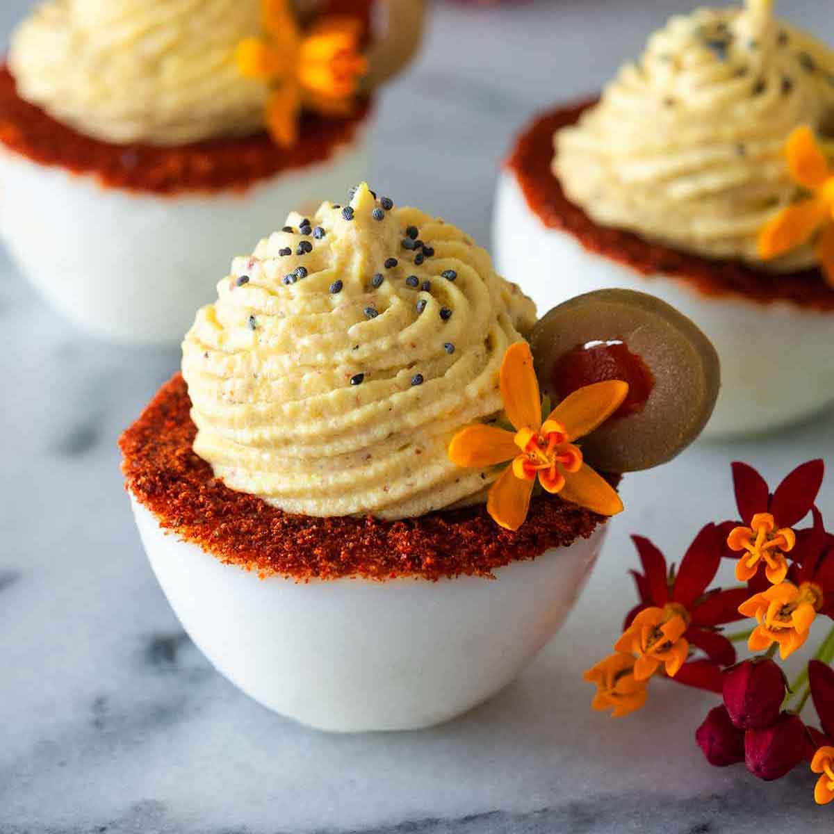 3 deviled eggs with spiced rims, garnished with olive slices and flowers.