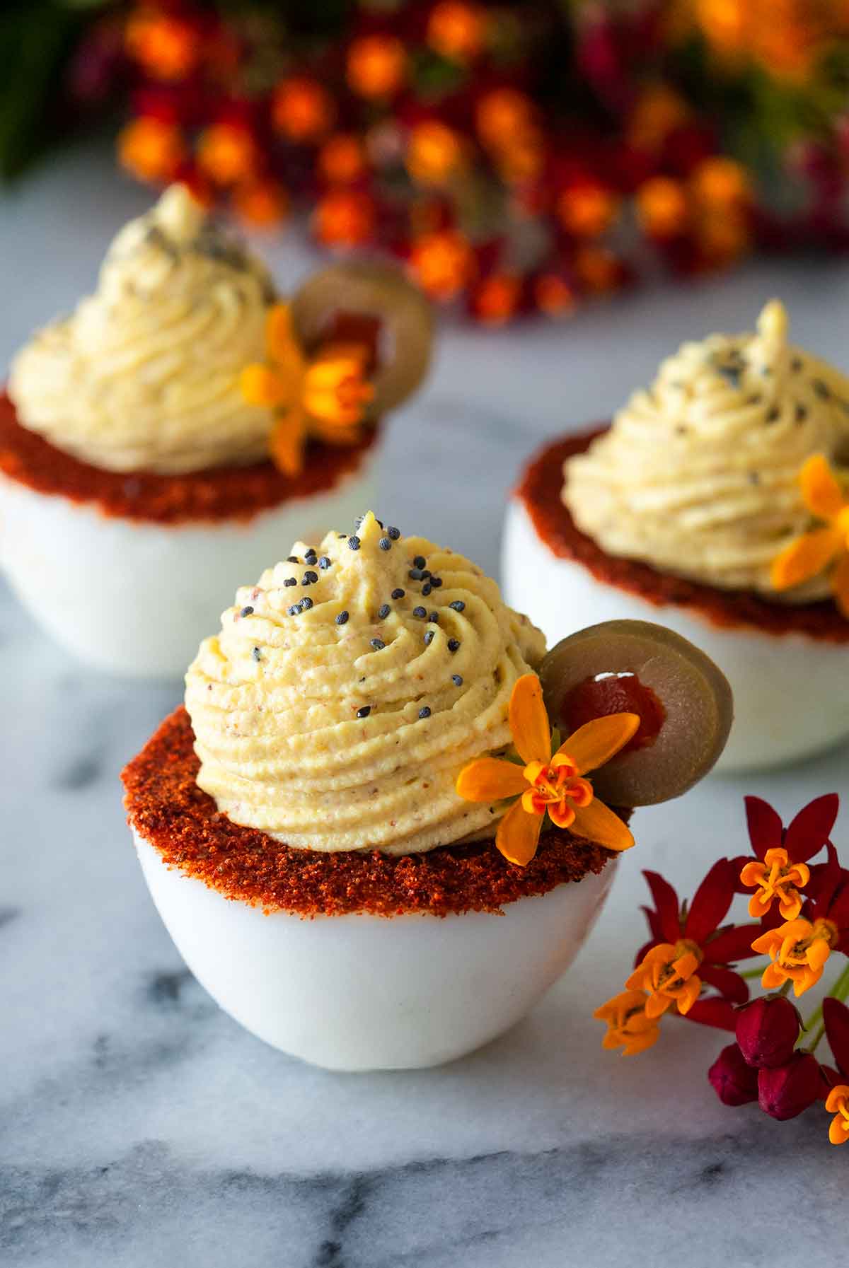 3 deviled eggs with spiced rims, garnished with olive slices and flowers.