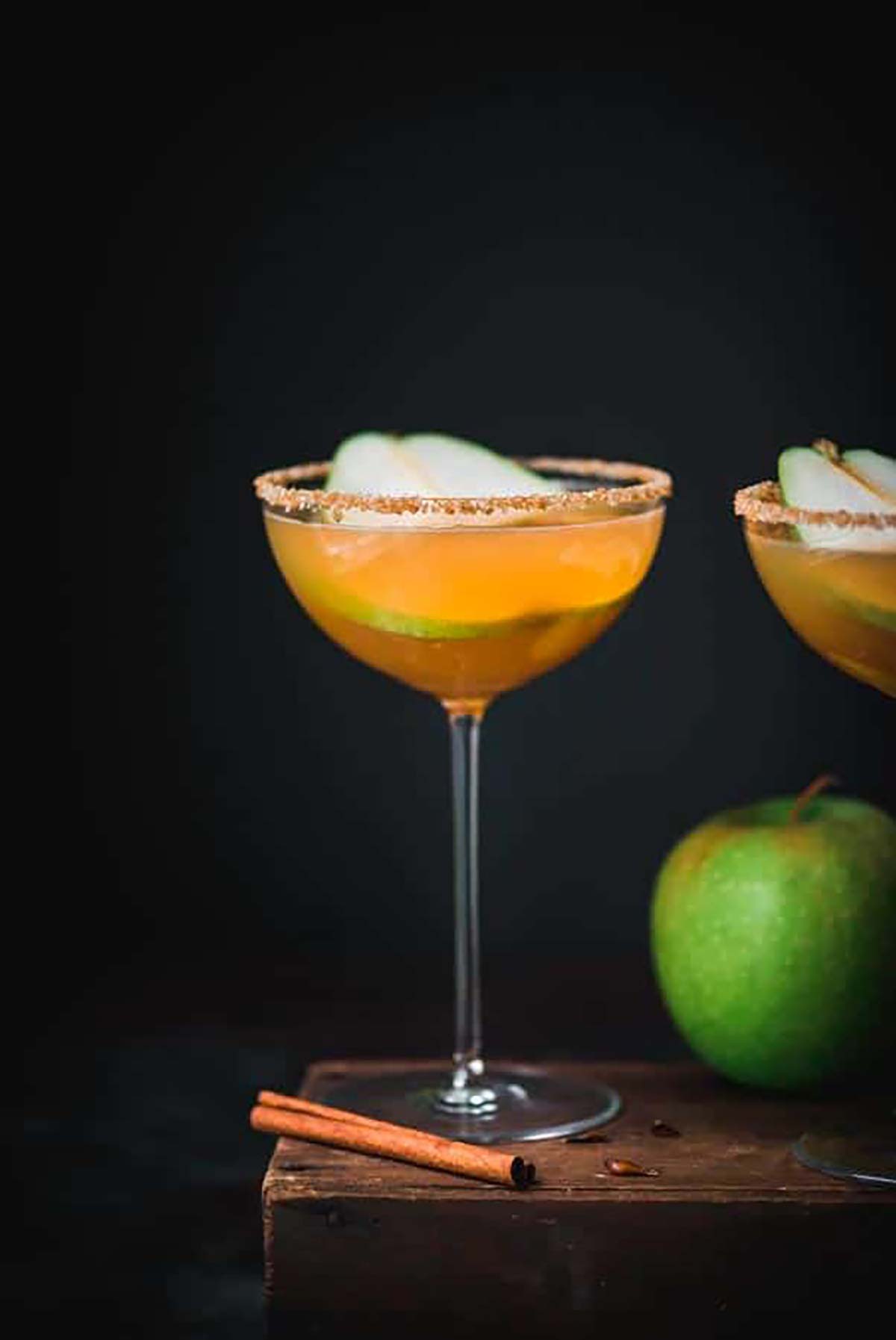 A martini garnished with a pear slice and a sugar rim beside a green apple.