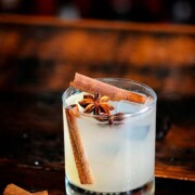 A cocktail garnished with cinnamon sticks and star anise on a table.