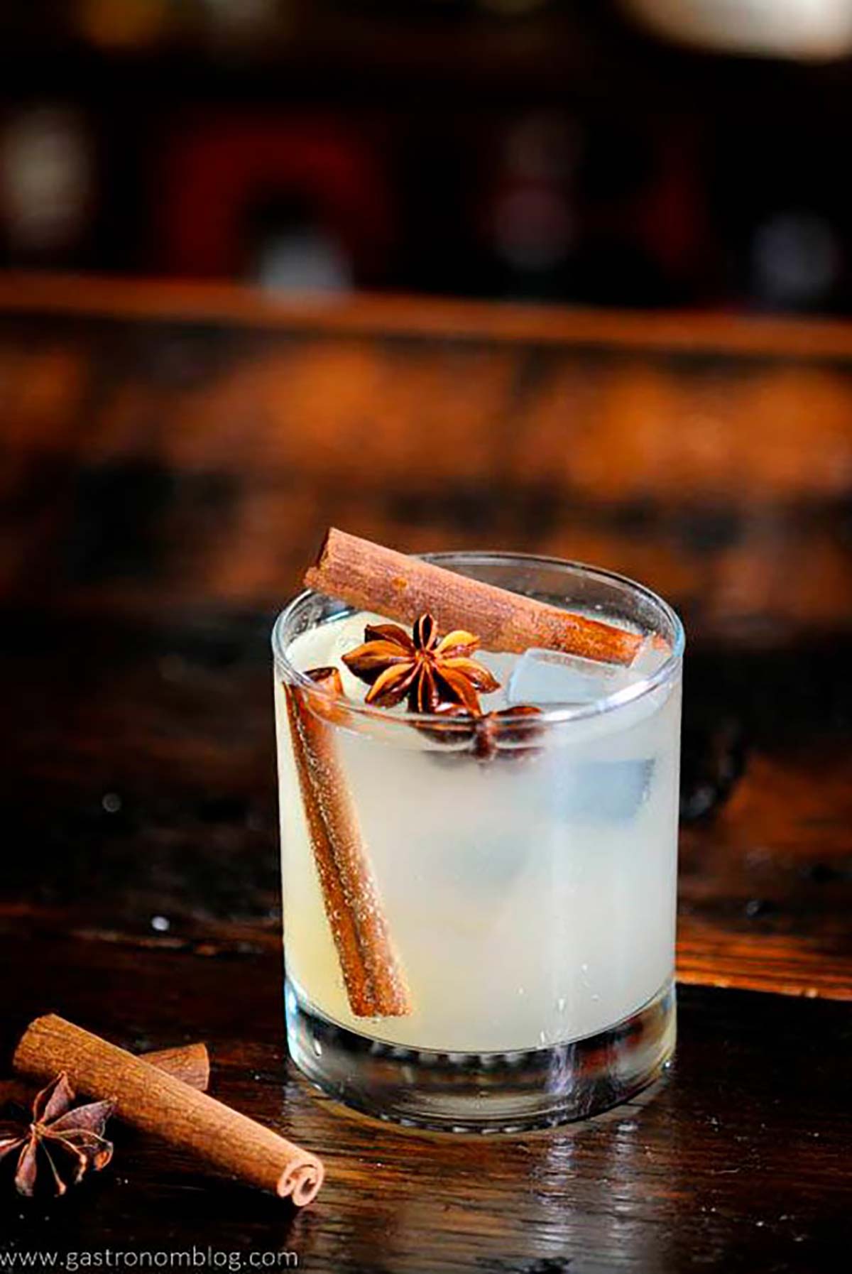 A cocktail garnished with cinnamon sticks and star anise on a table.