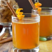 2 cocktails garnished with orange peels and cinnamon sticks.