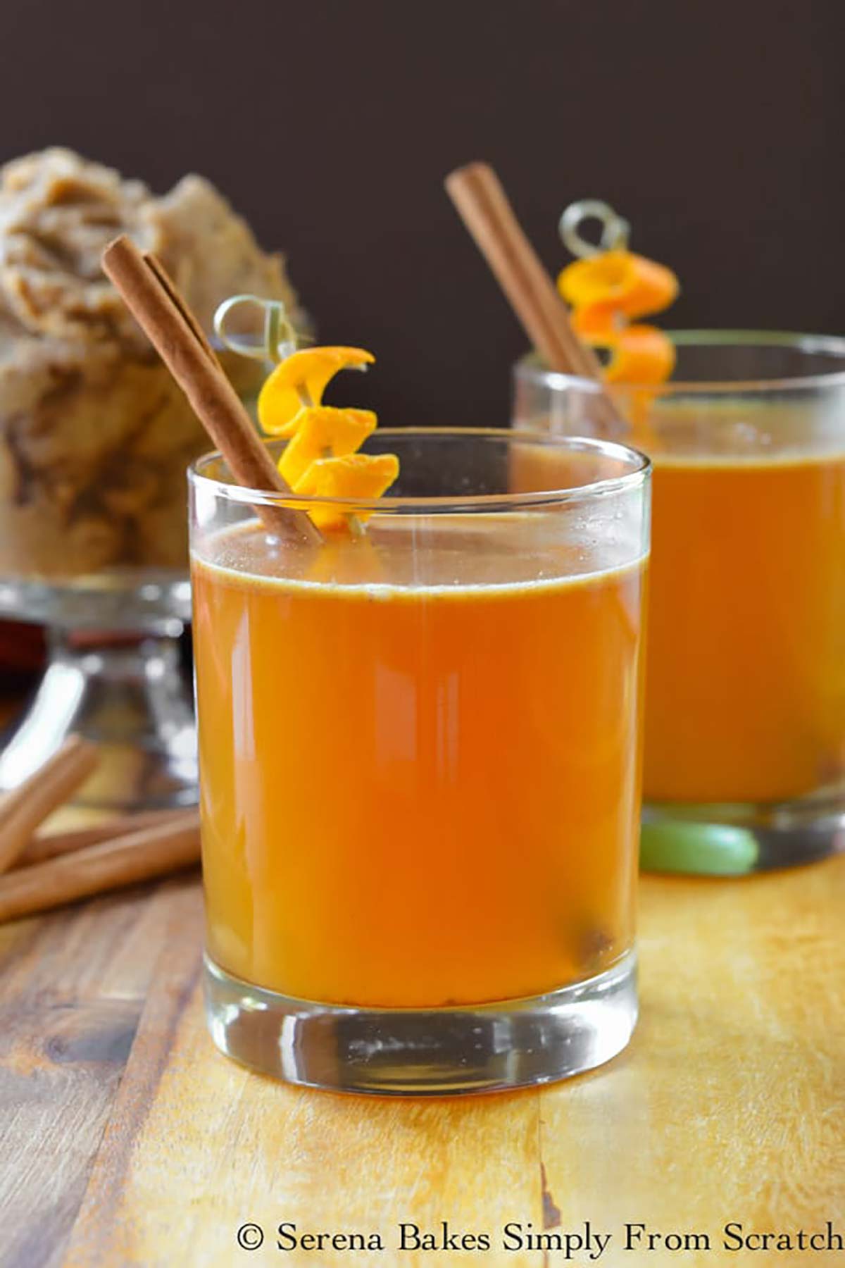 2 cocktails garnished with orange peels and cinnamon sticks.