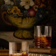 2 cocktails on a table in front of a dark floral print.