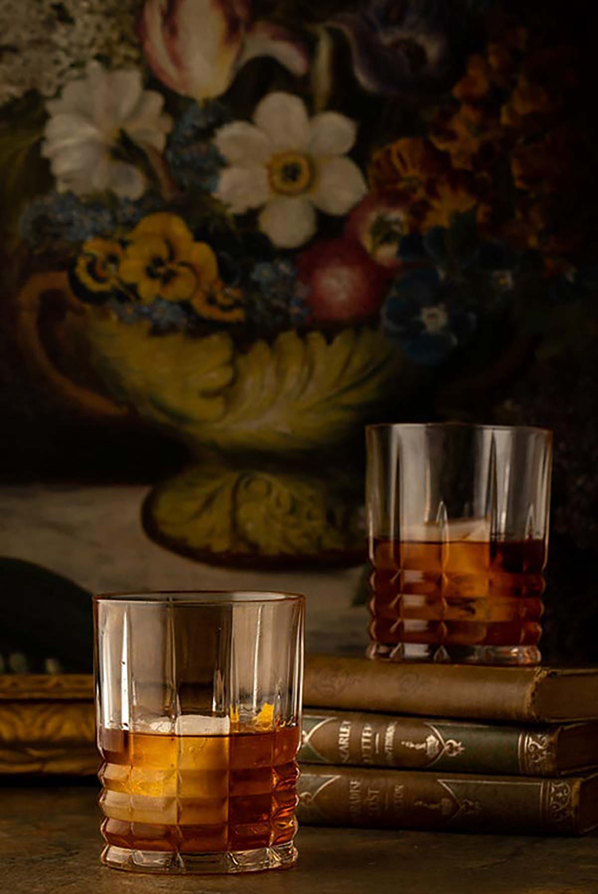 2 cocktails on a table in front of a dark floral print.