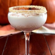 A cocktail in front of pumpkins, garnished with crumbs.