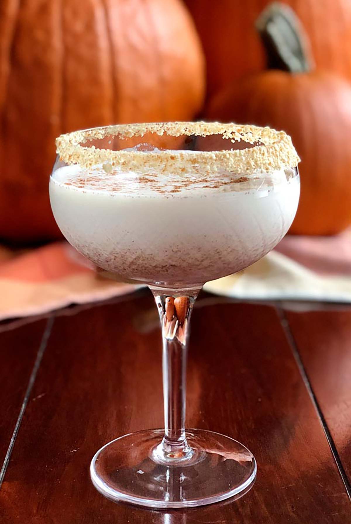 A cocktail in front of pumpkins, garnished with crumbs.