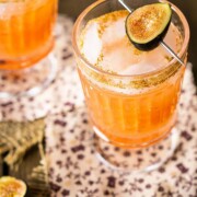 2 cocktails garnished with figs on a table with burlap and floral fabric coasters.