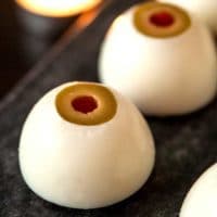 2 deviled eggs that look like eyeballs on a marble plate with a candle in the background.